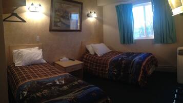 A hotel room with two beds, each with a different patterned bedspread, a bedside table with a lamp, a framed picture on the wall, and a window with curtains.