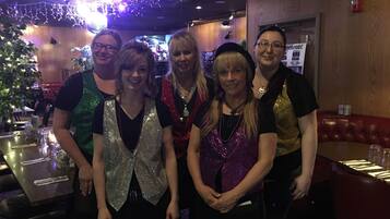 A group of people standing in a restaurant with wooden walls and a Christmas tree in the background.