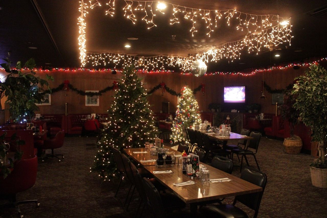 A restaurant with a Christmas tree, tables set for dining, and string lights on the ceiling.