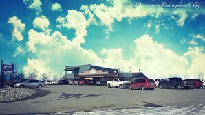 Un hotel con un estacionamiento amplio, un cartel que dice 'The Windbreak Hotel', y un cielo azul despejado con nubes.
