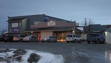 Un edificio con un letrero de restaurante, un estacionamiento con varios coches y suelo cubierto de nieve.