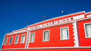 En röd byggnad med skylten ”HOTEL PINHEIRINHO” och många fönster.