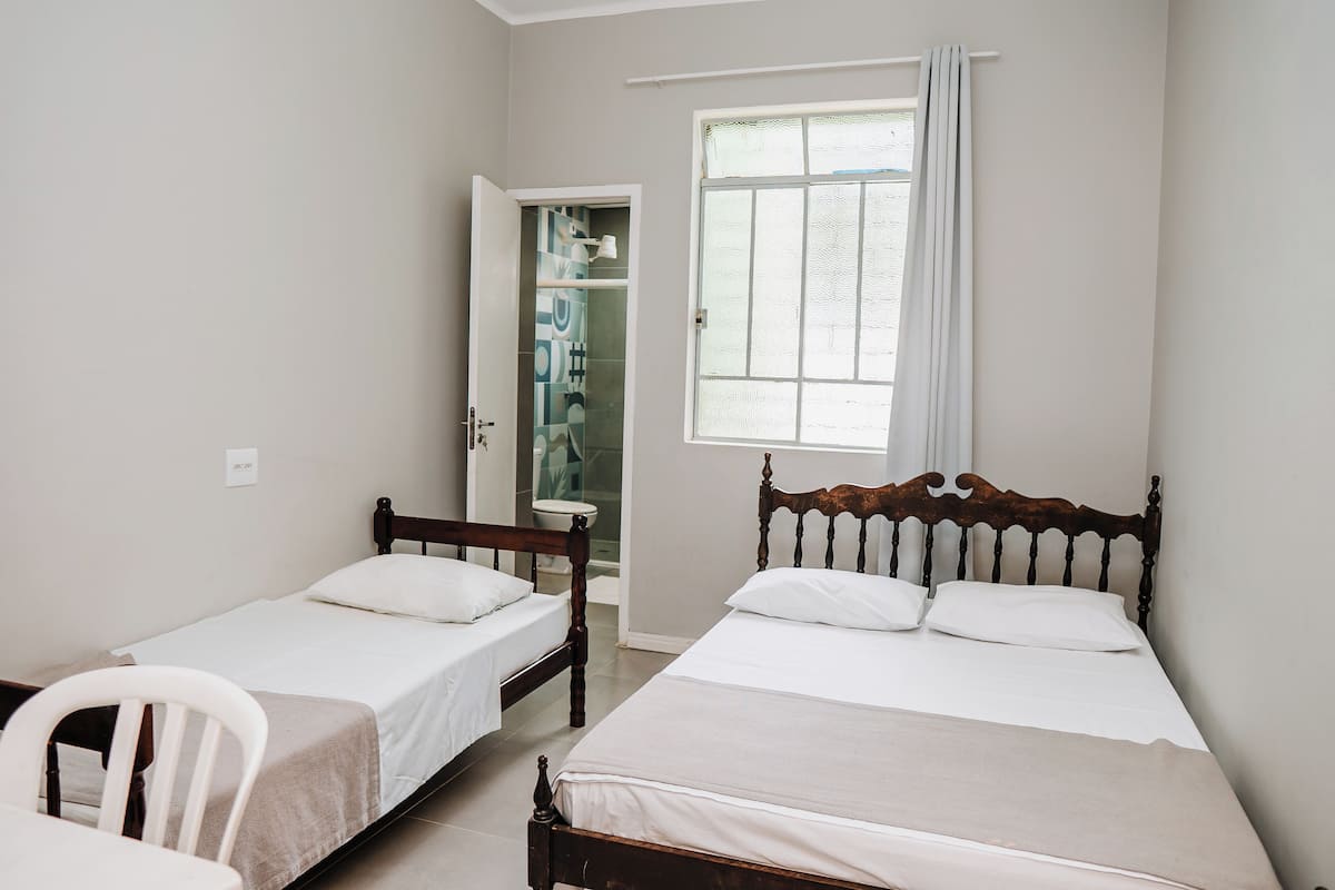 A bedroom with two single beds, a wooden chair, and a bathroom visible through an open door.