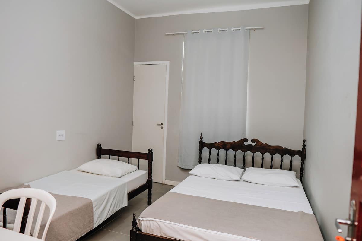 A bedroom with two single beds, a wooden headboard, a white chair, and a door with a curtain.