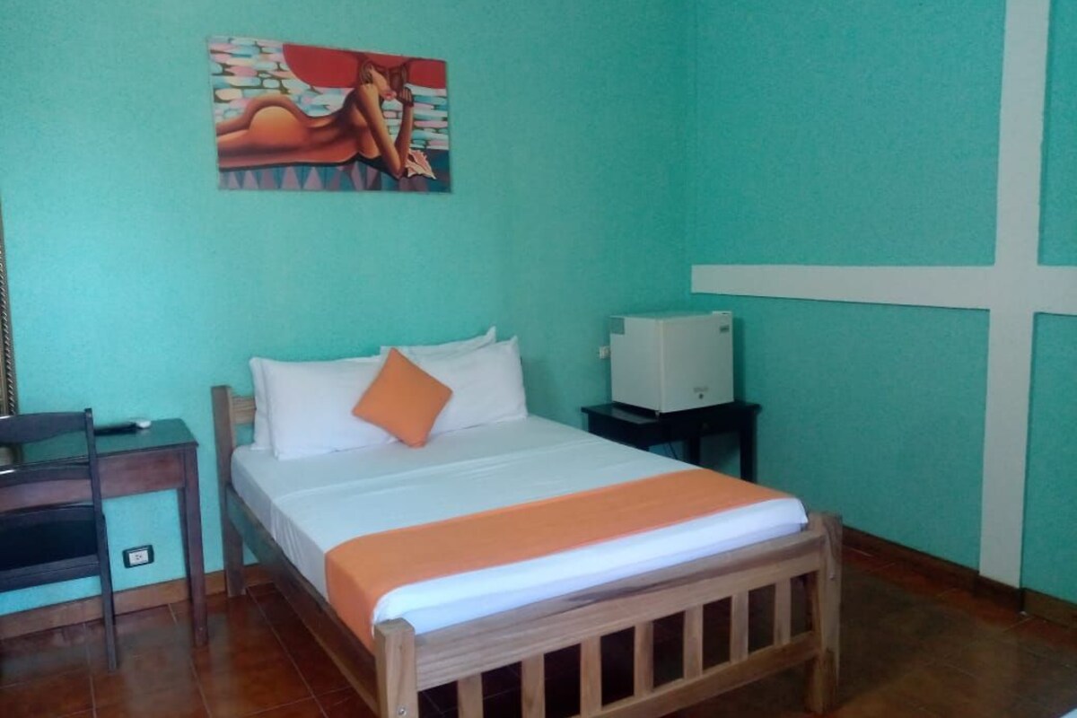 Una habitación con cama, mesita de noche, televisión y un cuadro en la pared.