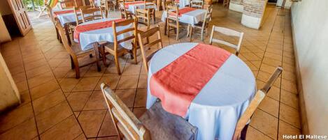 A spacious dining area with multiple tables and chairs, a tiled floor, and a rustic wooden ceiling.