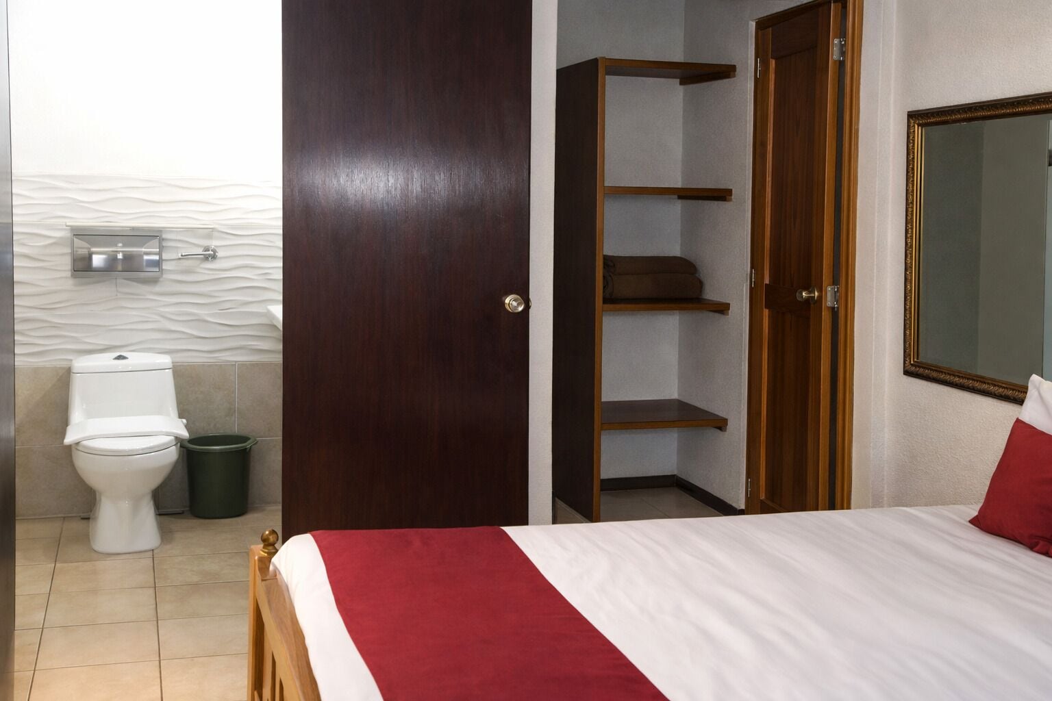Ein Schlafzimmer mit einem Bett, einem Holzschrank, einem Badezimmer mit Toilette und einem Spiegel.