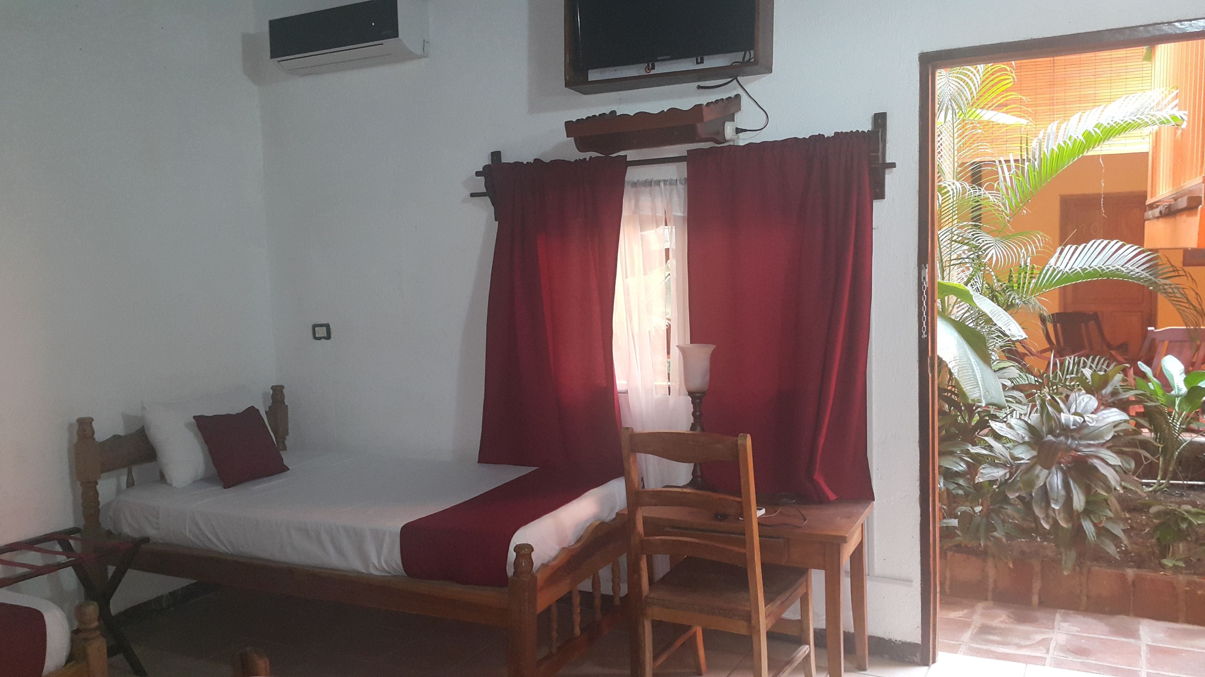 A bedroom with a bed, a chair, a TV, and a window with curtains.