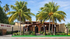 Un hotel con un letrero que dice 'HOTEL EL MALTSE', rodeado de palmeras y un techo de tejas.
