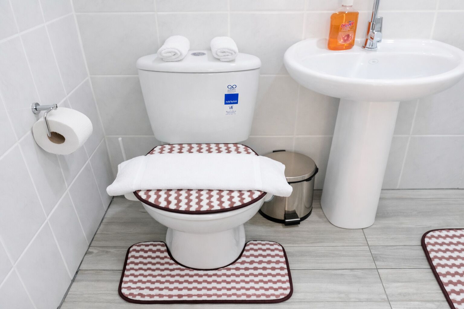 A bathroom with a toilet, a bidet, a sink, and a trash bin.