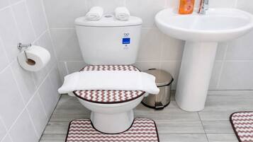 A bathroom with a toilet, a bidet, a sink, and a trash bin.