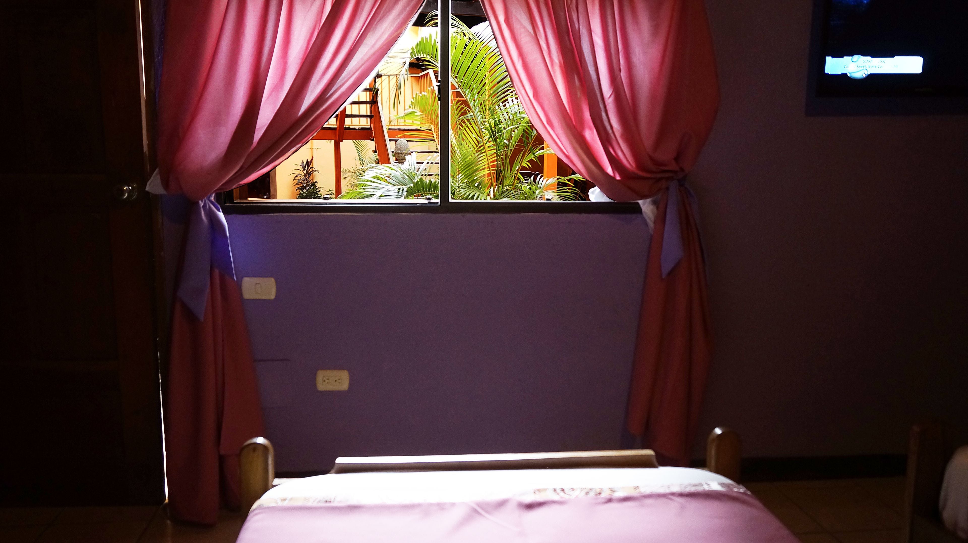 A room with a bed, purple walls, and a window with curtains.