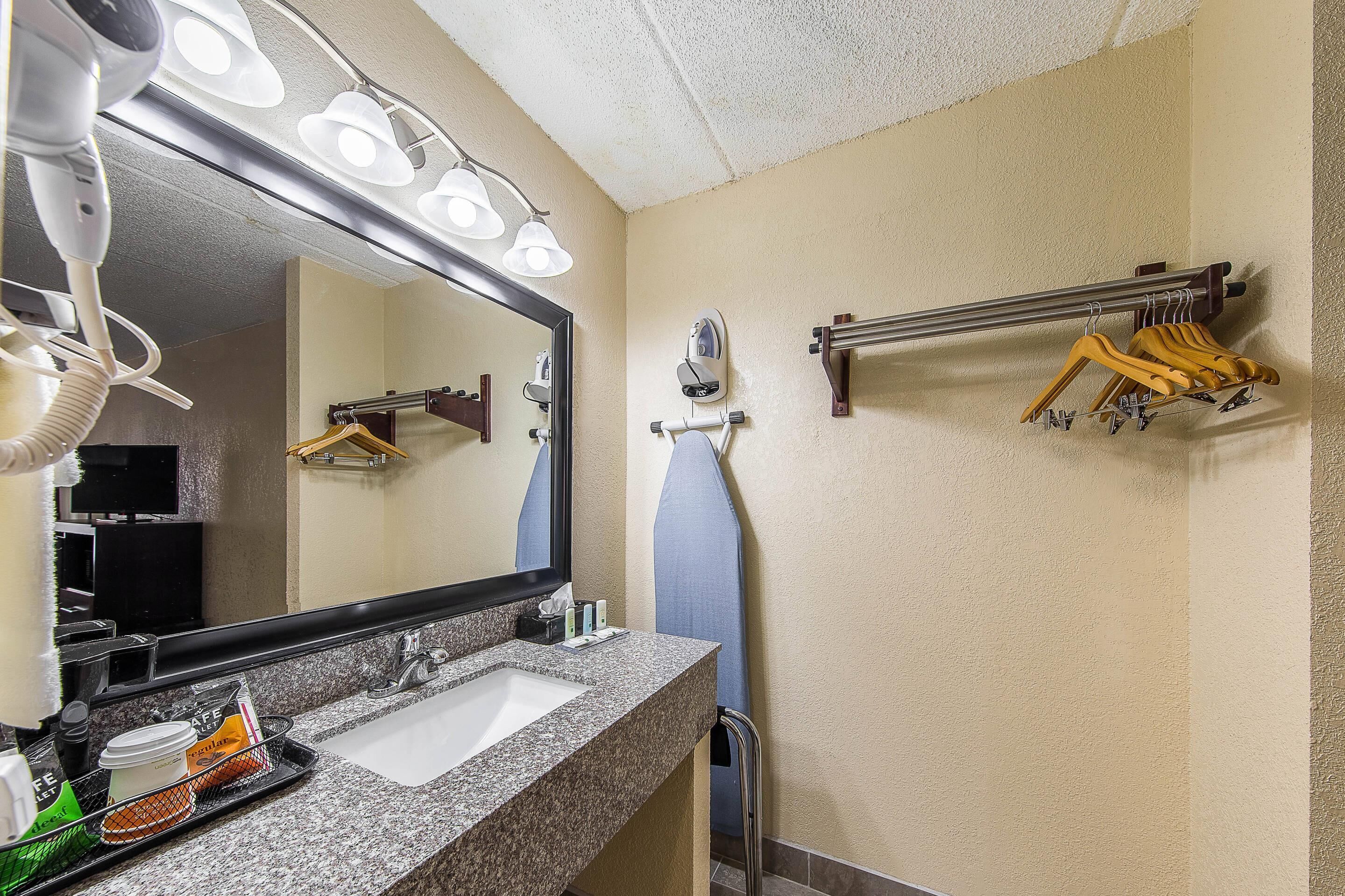 A bathroom with a sink, mirror, hairdryer, towel rack, and a towel hanging on the wall.