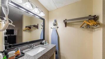 A bathroom with a sink, mirror, hairdryer, towel rack, and a towel hanging on the wall.