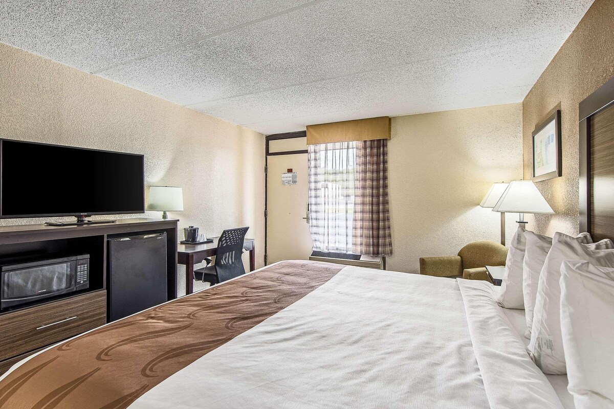Una habitación de hotel con una cama, un escritorio con televisor, un microondas y un refrigerador.