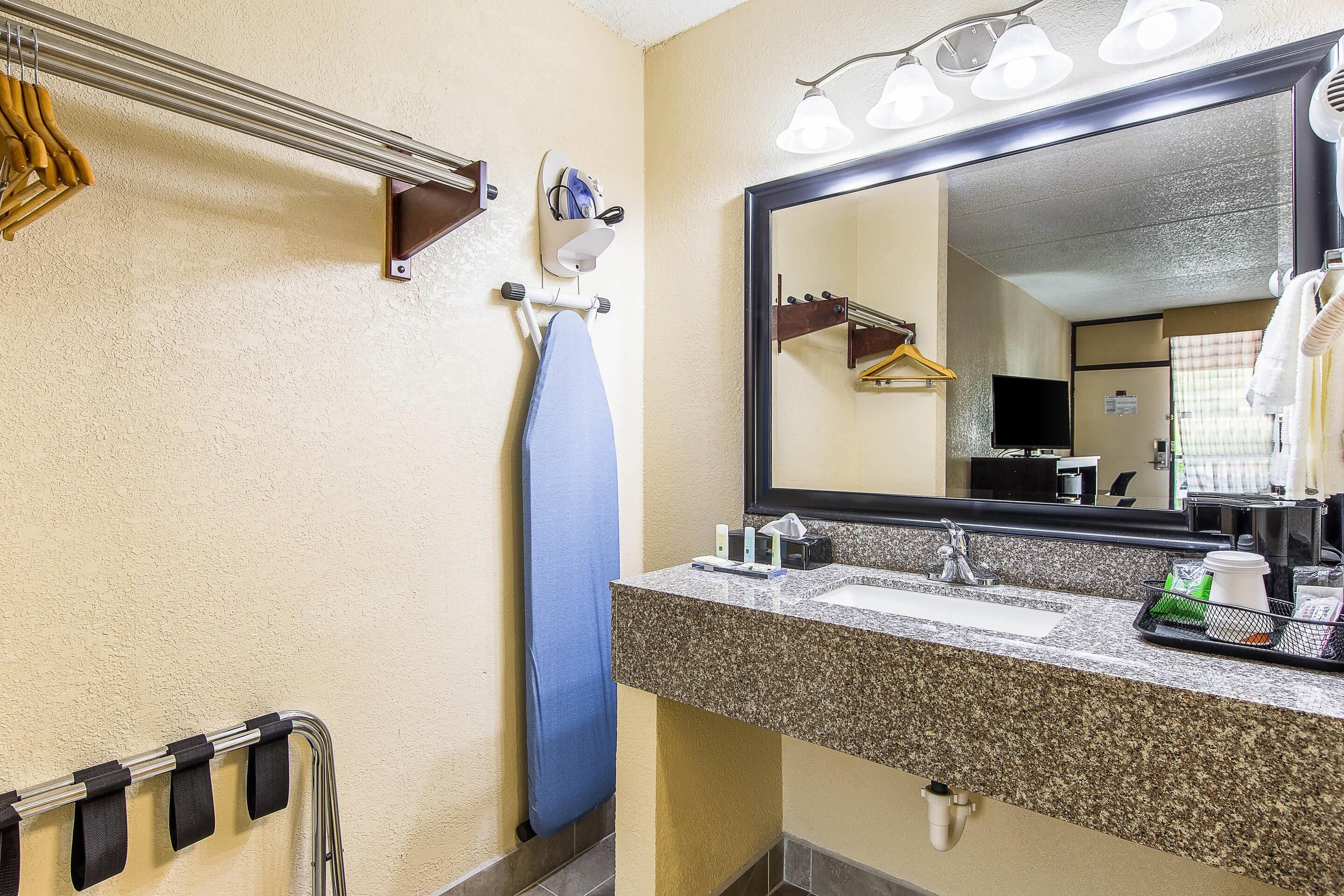 A hotel bathroom with a granite countertop, a sink, a mirror, and a towel rack.