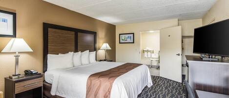 A hotel room with a large bed, bedside lamps, a desk with a telephone, a television, and a carpeted floor.