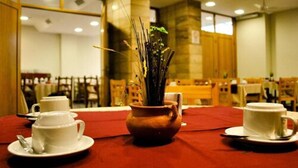 Comedor con una mesa preparada para dos personas, con un florero con follaje y dos tazas blancas sobre platillos.