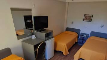 Habitación de hotel con dos camas individuales, un escritorio con computadora, un refrigerador pequeño y un ventilador de techo.