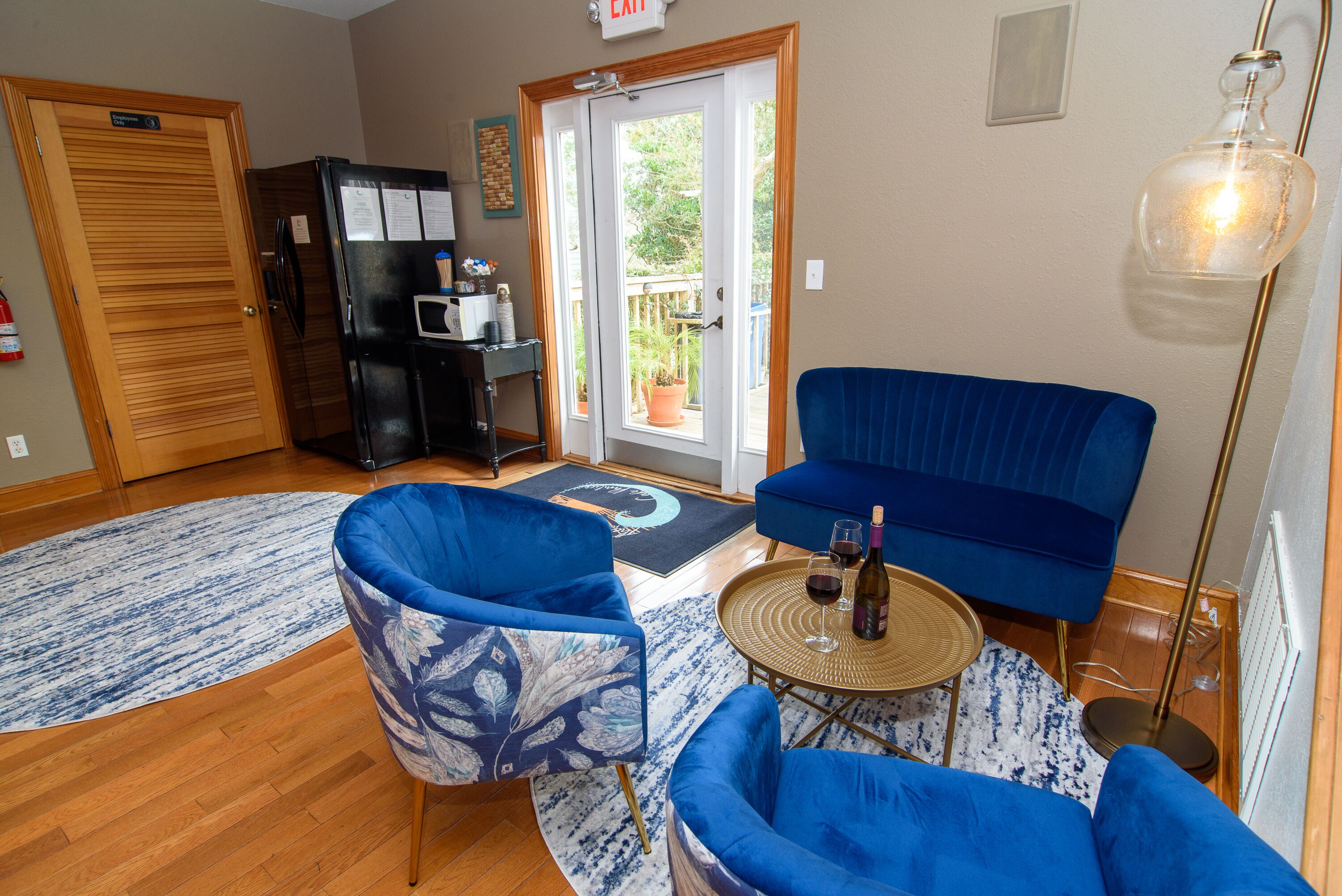 A living room with blue furniture, a black refrigerator, a wooden door, and a view through a glass door.