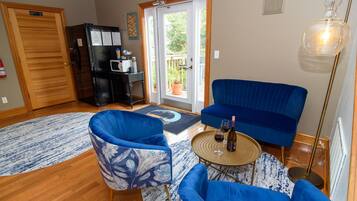 A living room with blue furniture, a black refrigerator, a wooden door, and a view through a glass door.