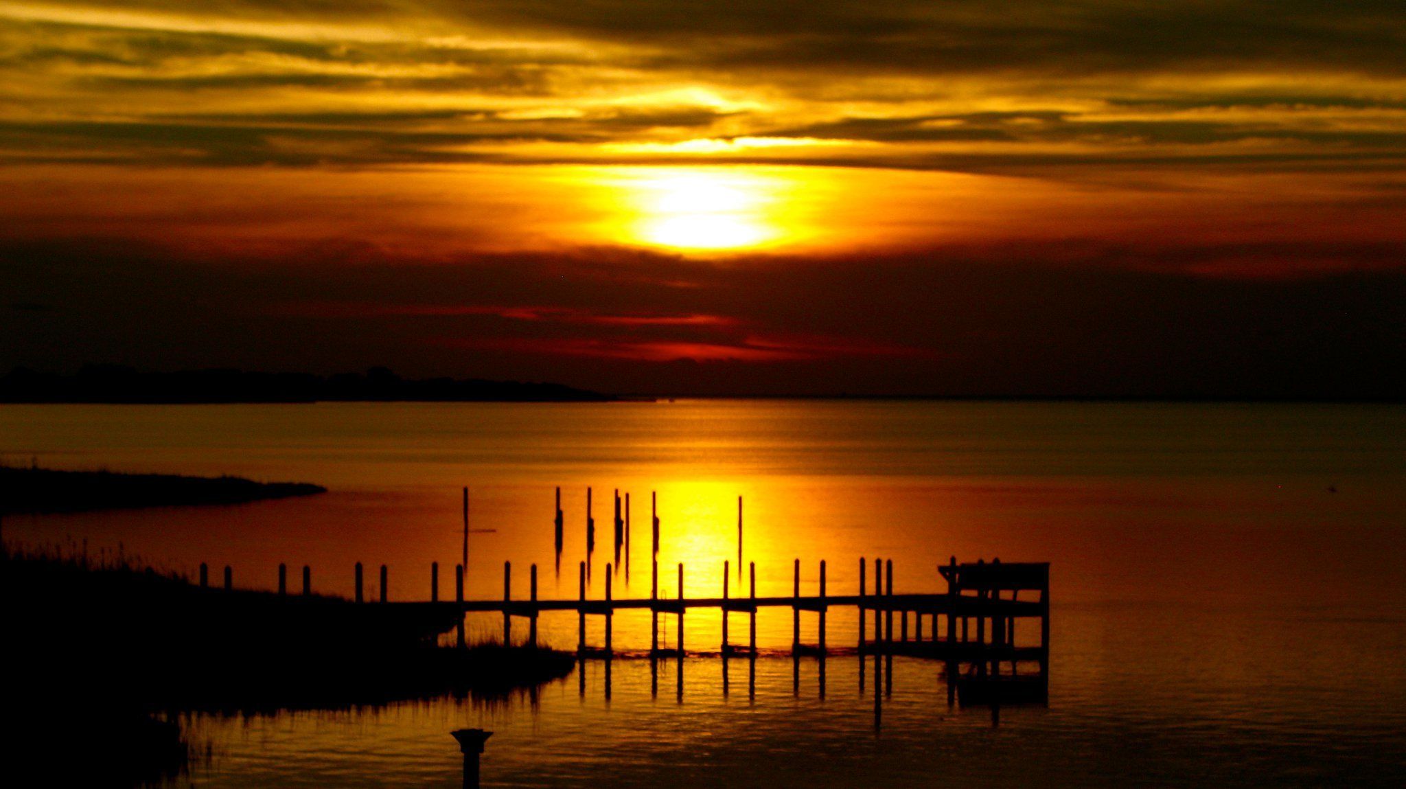A sunset over a calm body of water with a dock extending into the water.