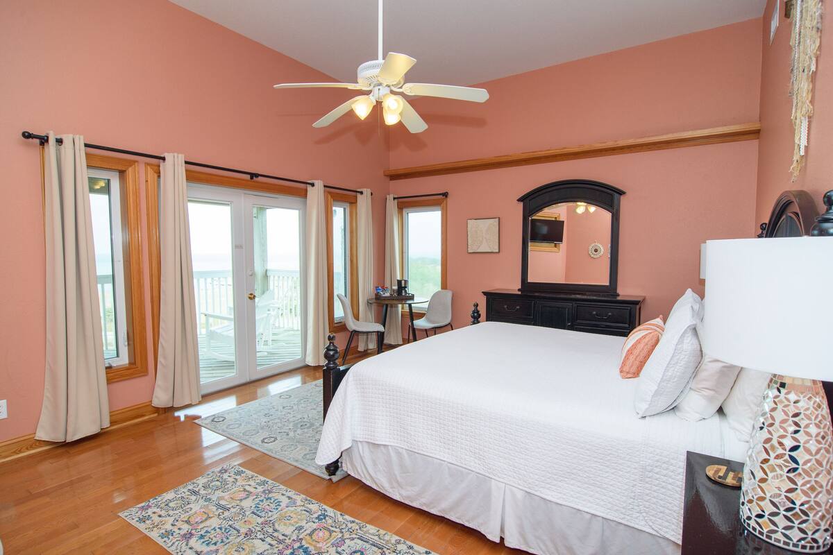 A bedroom with a large bed, a ceiling fan, a dresser, a desk, and a chair.