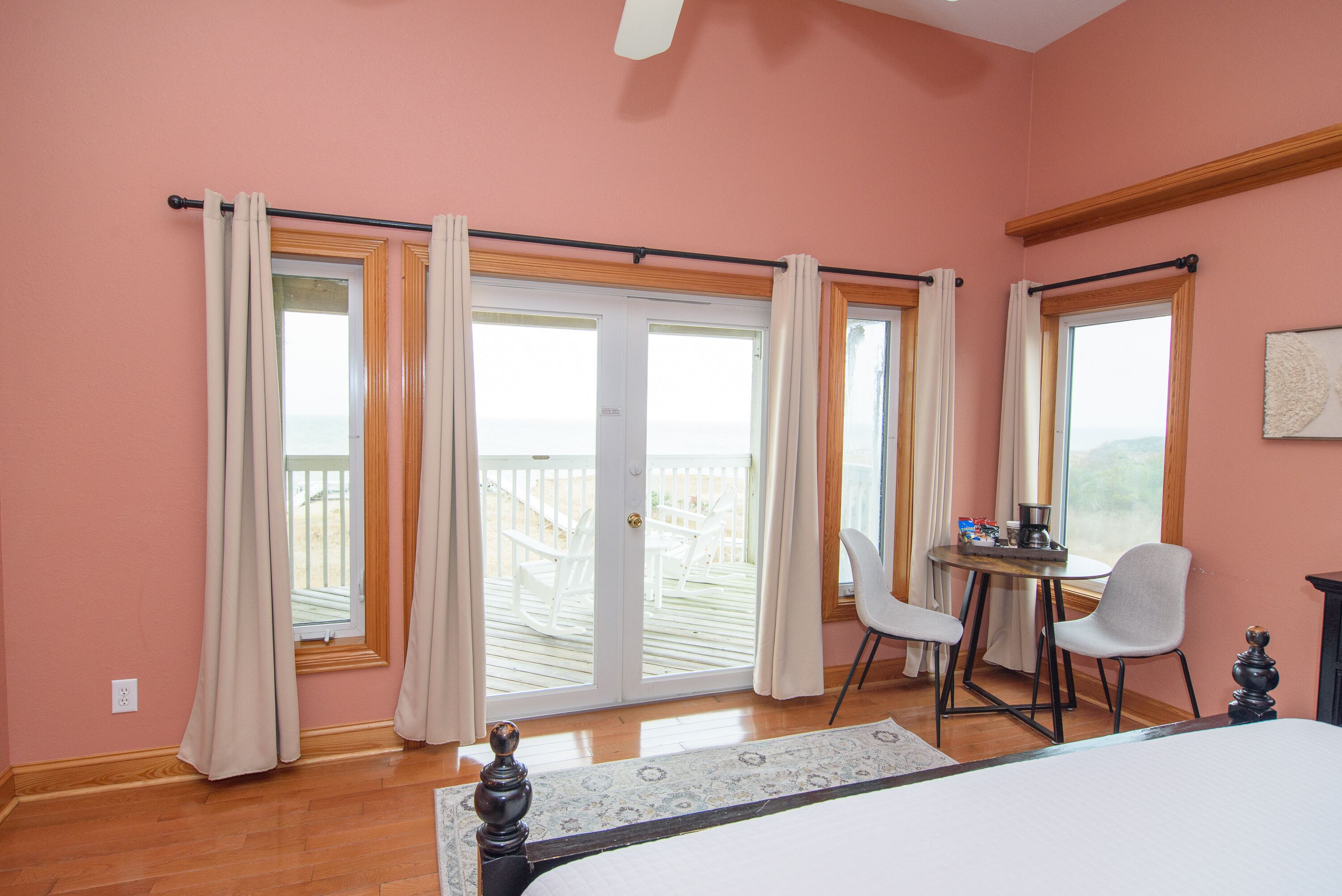Quarto com uma cama grande, uma escrivaninha com cadeira e vista para um terraço através de uma porta de correr de vidro.