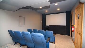 Una sala de cine en casa con seis sillas azules, piso alfombrado, una pantalla blanca y una puerta de madera.