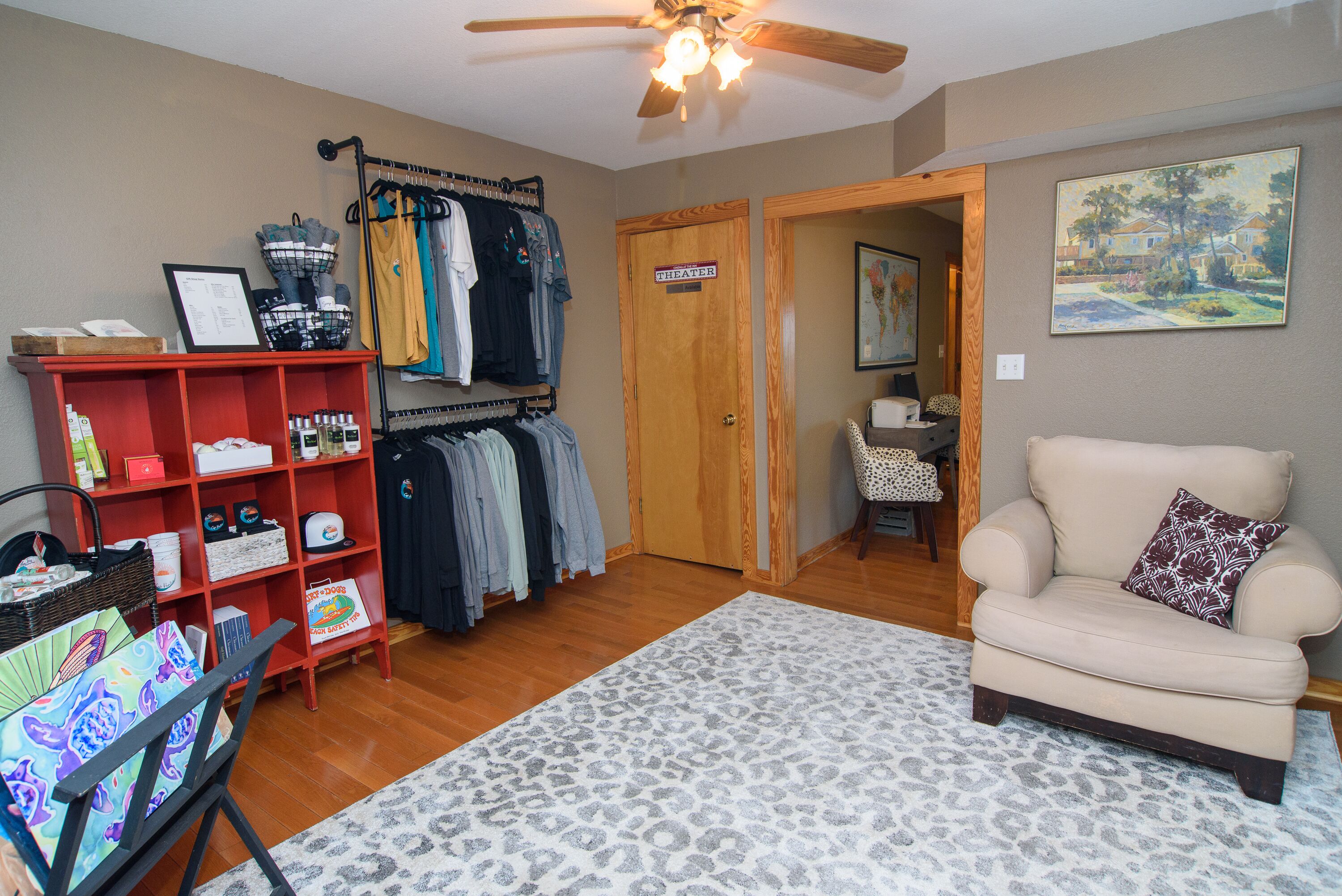 A room with a wooden floor, a beige armchair, a red shelf unit, a clothing rack, and a door labeled "THEATER".