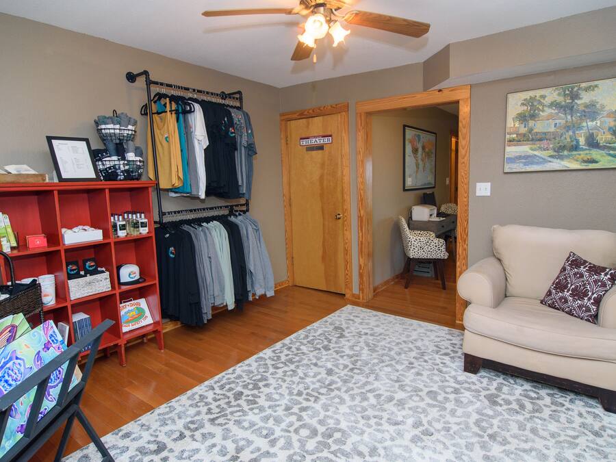 A room with a wooden floor, a beige armchair, a red shelf unit, a clothing rack, and a door labeled "THEATER".