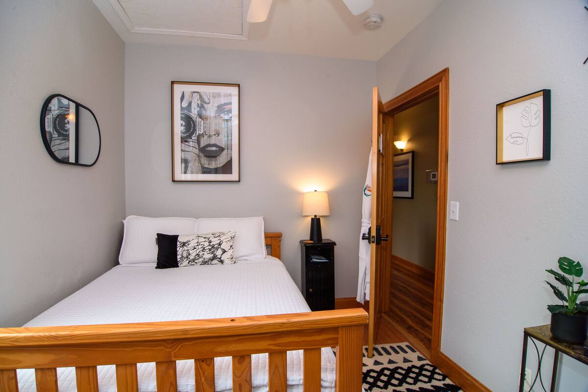 A bedroom with a bed, a bedside lamp, a mirror, and framed artwork on the wall.