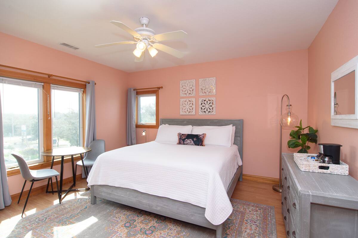 A bedroom with a bed, a desk, a chair, a ceiling fan, and a window with curtains.