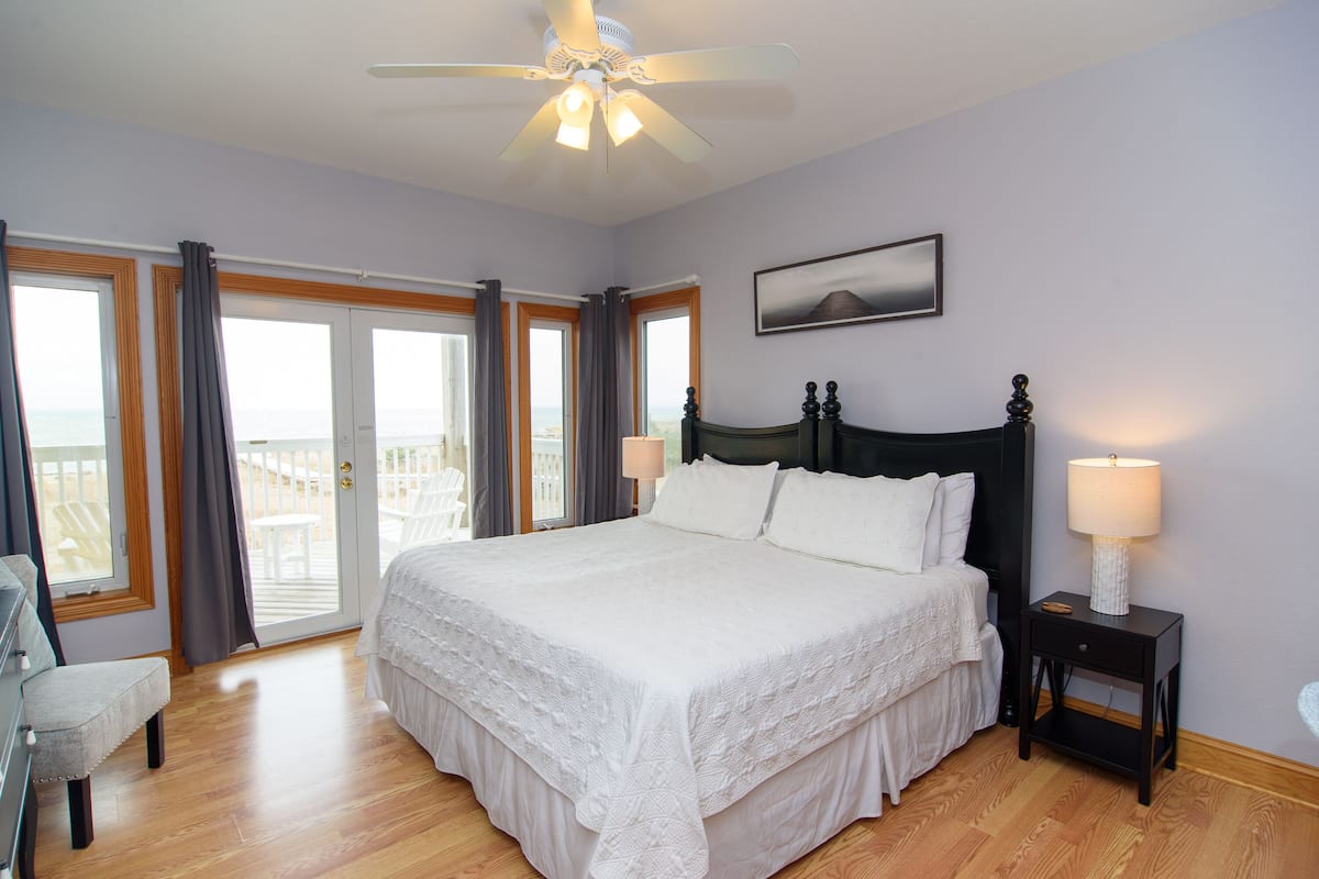 A bedroom with a large bed, a nightstand, a ceiling fan, and a view through the glass doors.