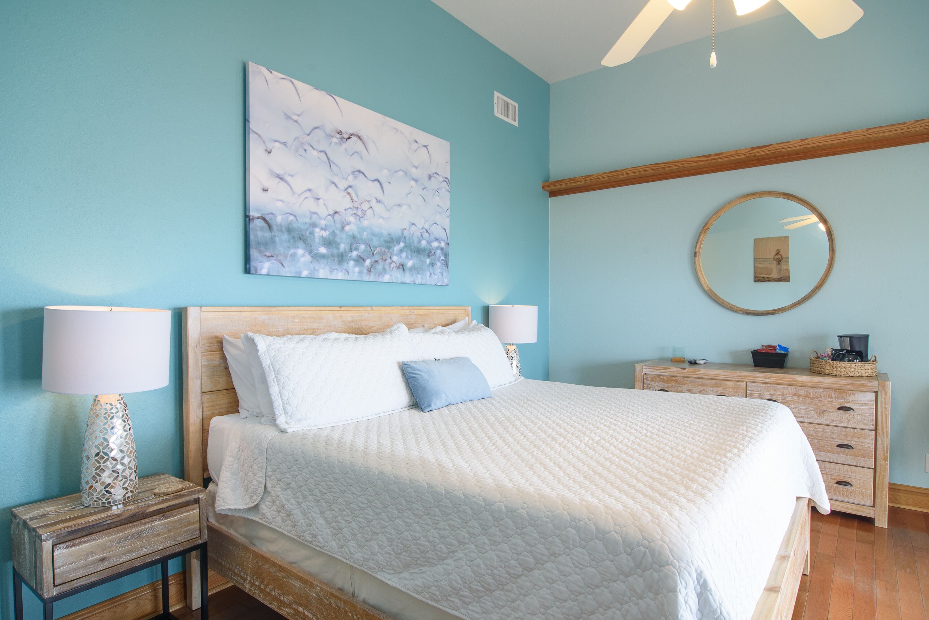 Un dormitorio con cama, mesitas de noche, cómoda, espejo y un cuadro en la pared.