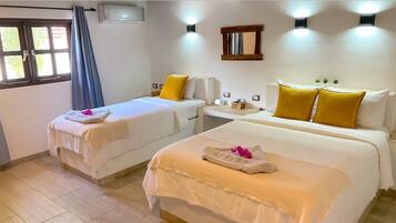 Une chambre d’hôtel avec deux lits, chacun doté de draps blancs et d’oreillers jaunes, une petite table de chevet, un climatiseur fixé au mur et une fenêtre avec des rideaux.
