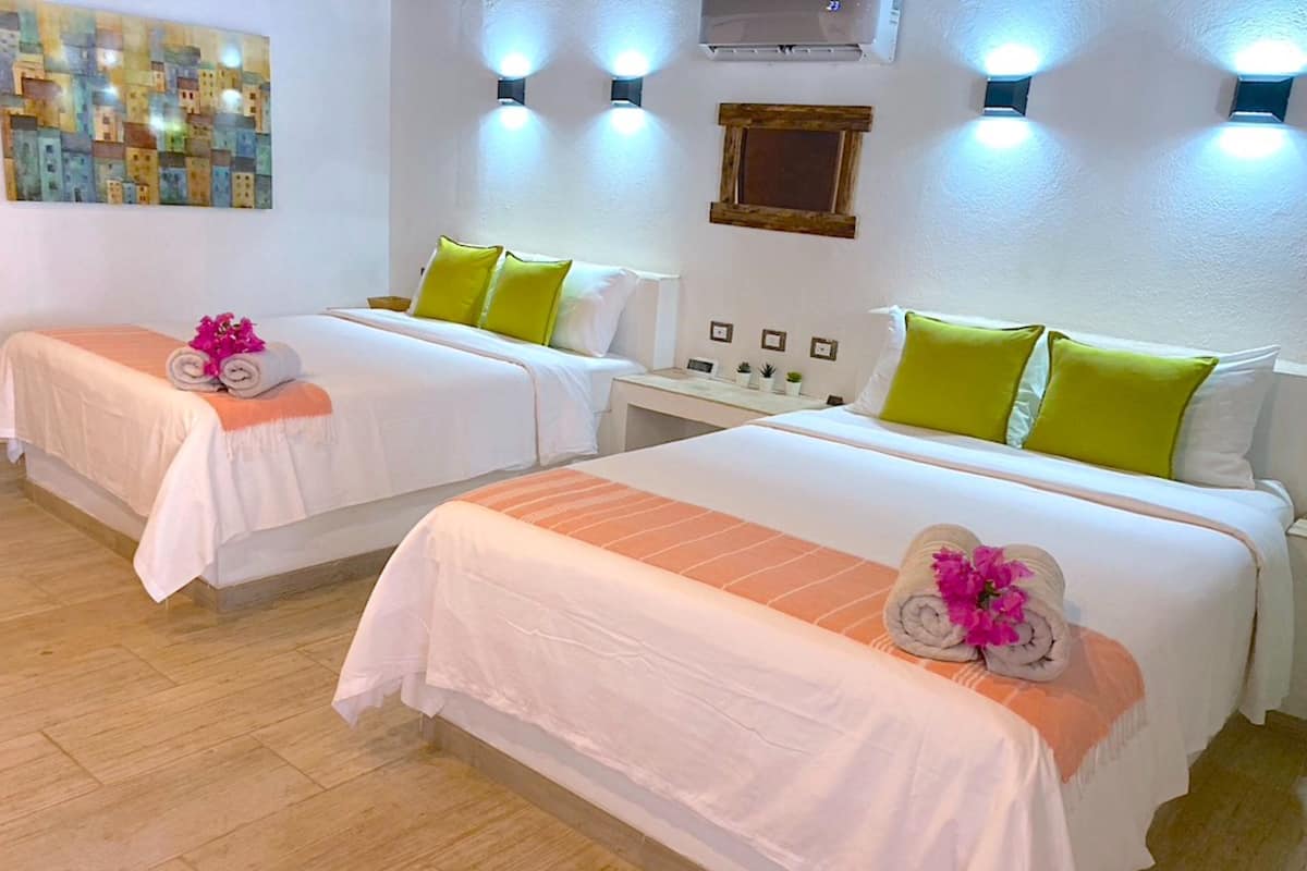 Dos camas individuales con ropa blanca y almohadas verdes, una mesita con espejo y un aire acondicionado instalado en la pared.