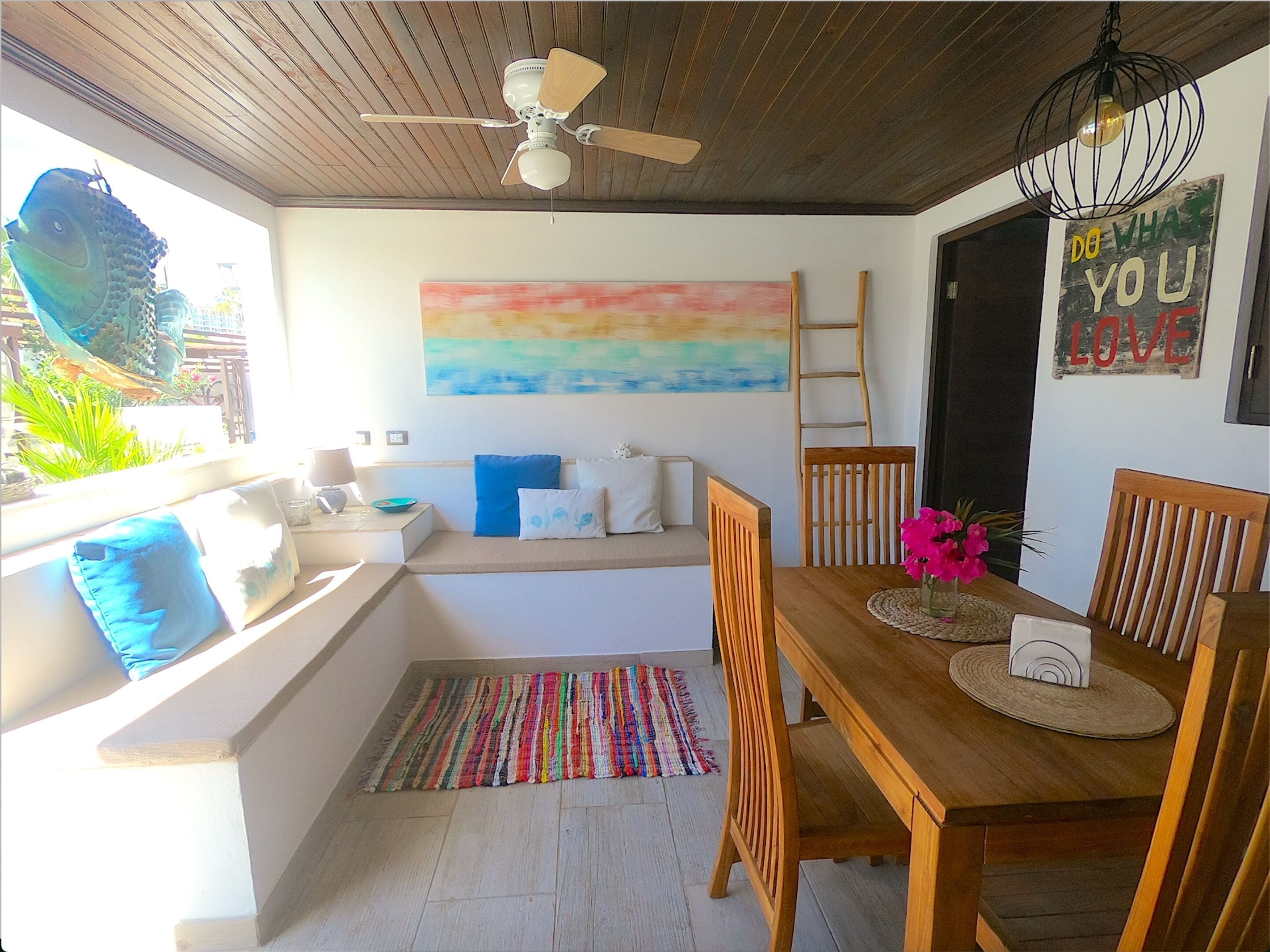 A cozy dining area with a wooden table and chairs, a colorful rug, and a ceiling fan.
