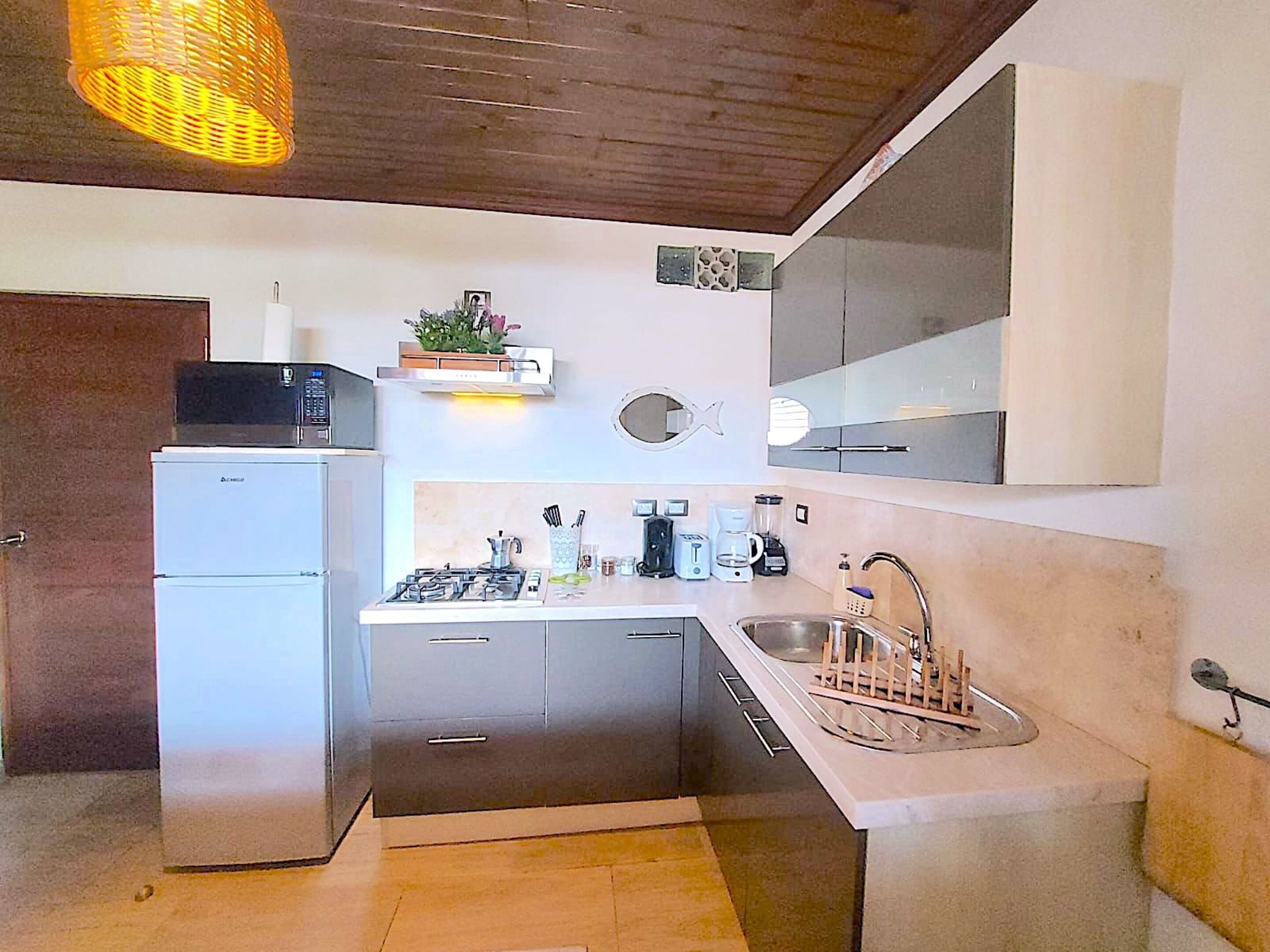 Cocina compacta con refrigerador, estufa, lavamanos y una lámpara colgante.