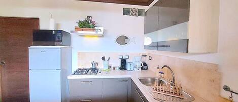 Cocina compacta con refrigerador, estufa, lavamanos y una lámpara colgante.