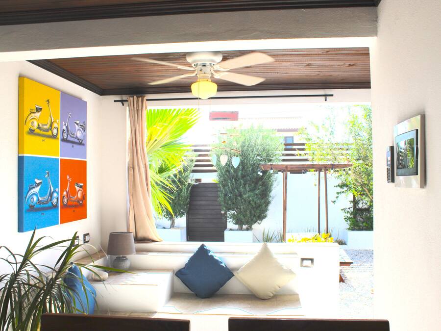 Un salon moderne doté d’un ventilateur de plafond, d’un canapé avec des coussins, d’une table basse et offrant une vue sur le jardin extérieur.