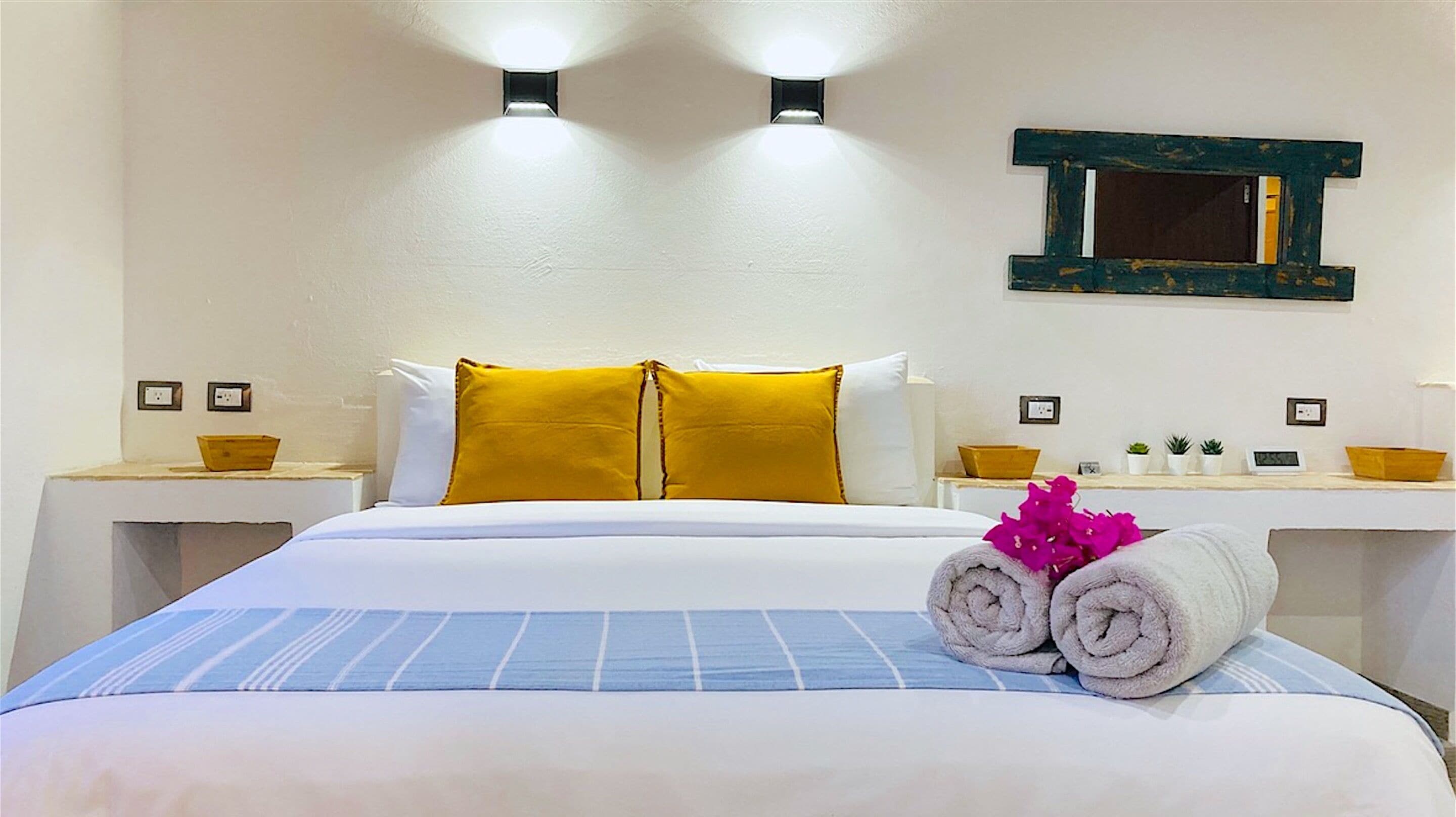 A hotel room with a bed, two bedside tables, a mirror, and a small shelf with toiletries.