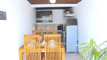 Un comedor con una mesa y sillas de madera, un ventilador de techo y una cocina al fondo.