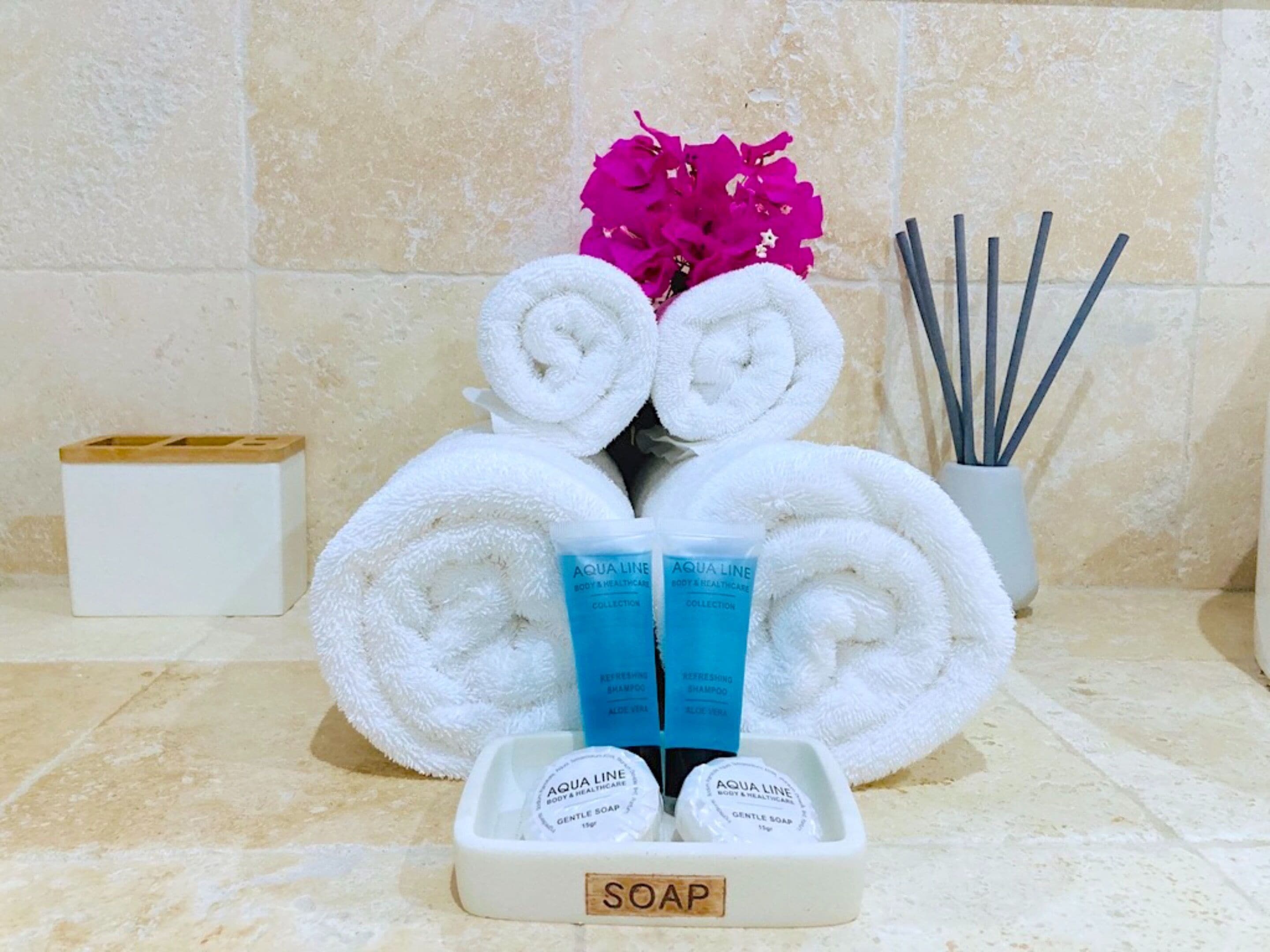 Un baño con artículos de aseo, incluyendo toallas enrolladas, un jabonera y un recipiente con ramitas de junco.