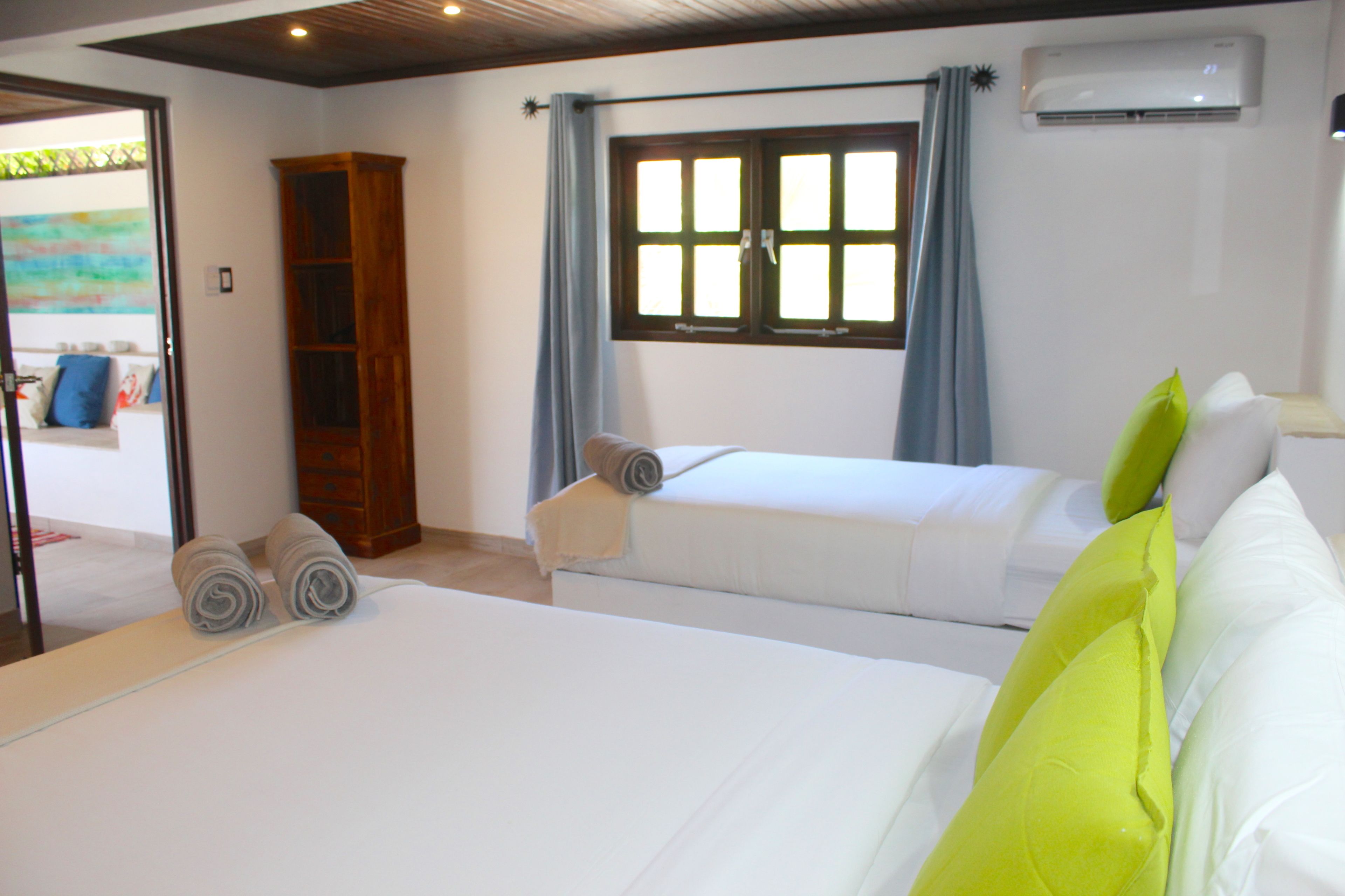 Ein Hotelzimmer mit zwei Betten, einem Kleiderschrank, einem Fenster mit Vorhängen und einer Klimaanlage.