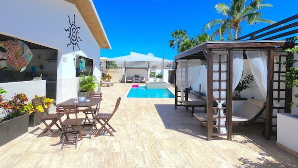 Zona de piscina con pérgola, mobiliario exterior y vista a la piscina.