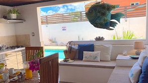 Una sala moderna con vista a una piscina, un comedor con alimentos para el desayuno y un gran pez decorativo colgado del techo.