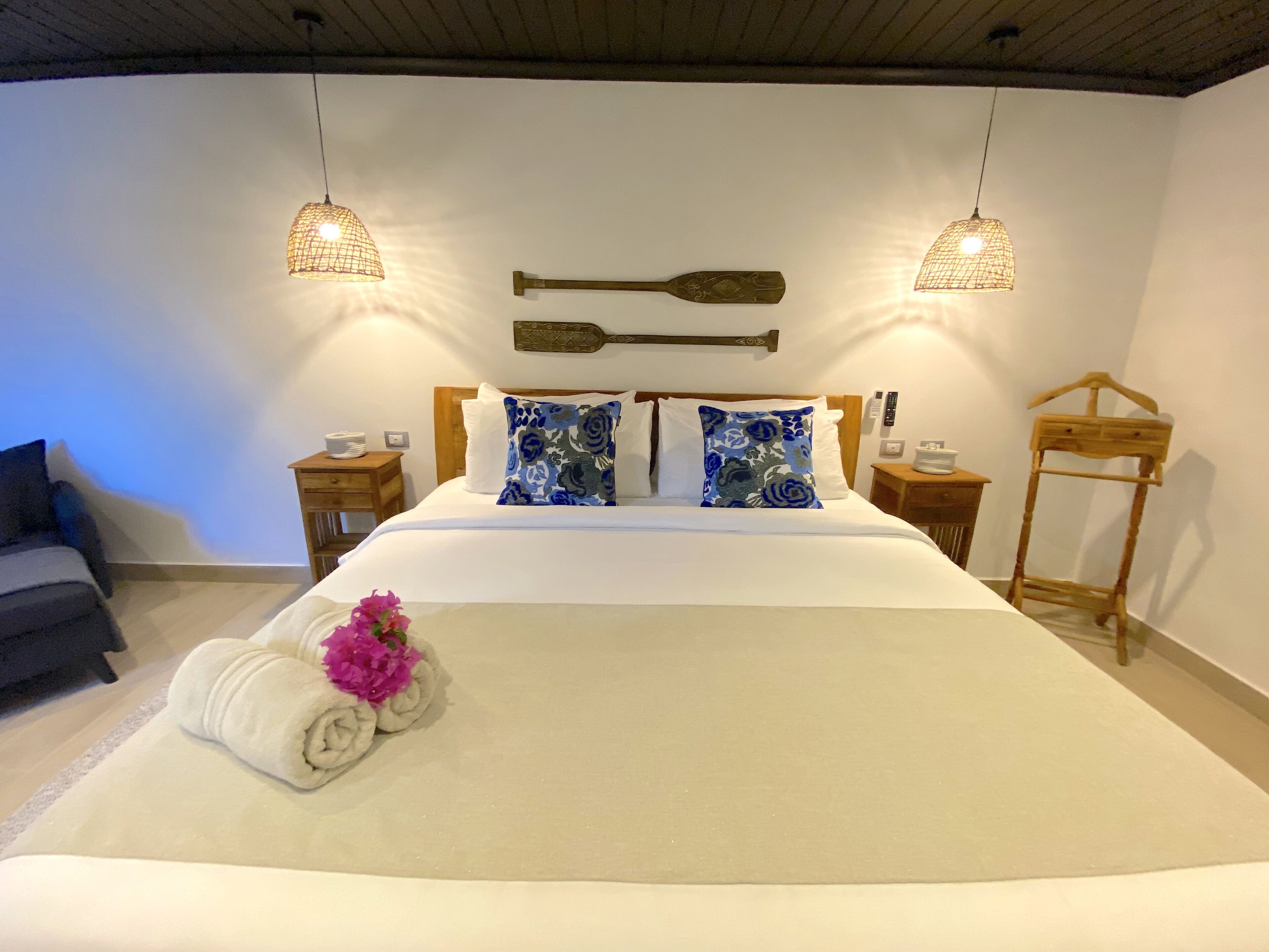 Una cama bien hecha con sábanas blancas, dos almohadas decorativas, un cabecero de madera y dos mesitas de noche con lámparas.