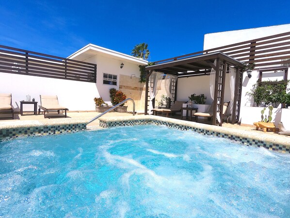 A swimming pool with a tiled edge, lounge chairs, and a covered seating area with a pergola.