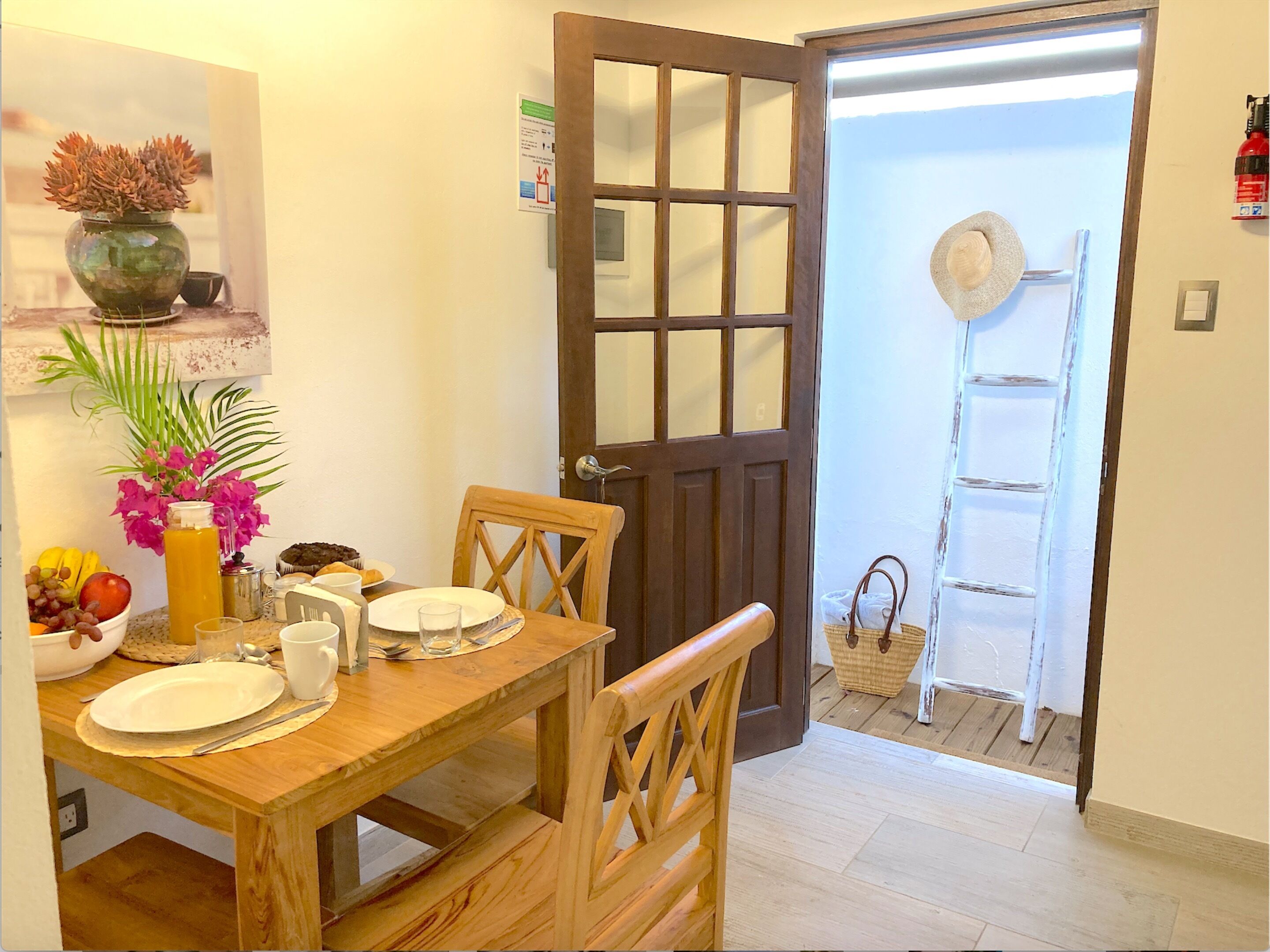 A dining area with a wooden table set for two, a vase with flowers, and a fruit bowl.